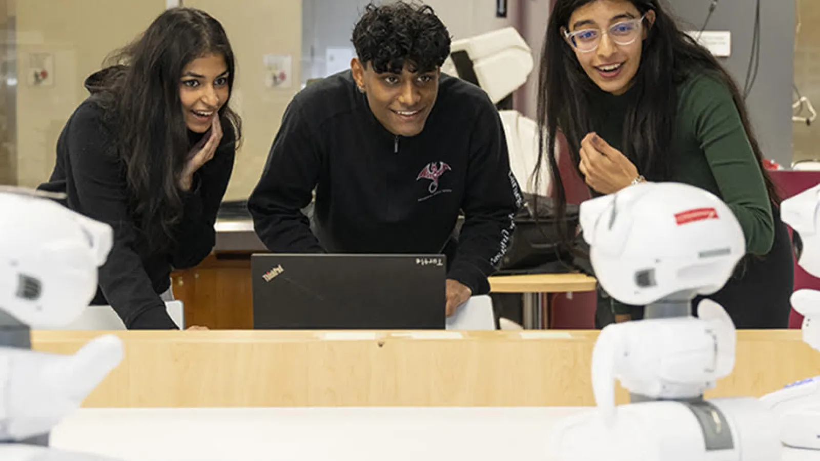 Three students looking at a robot and smiling